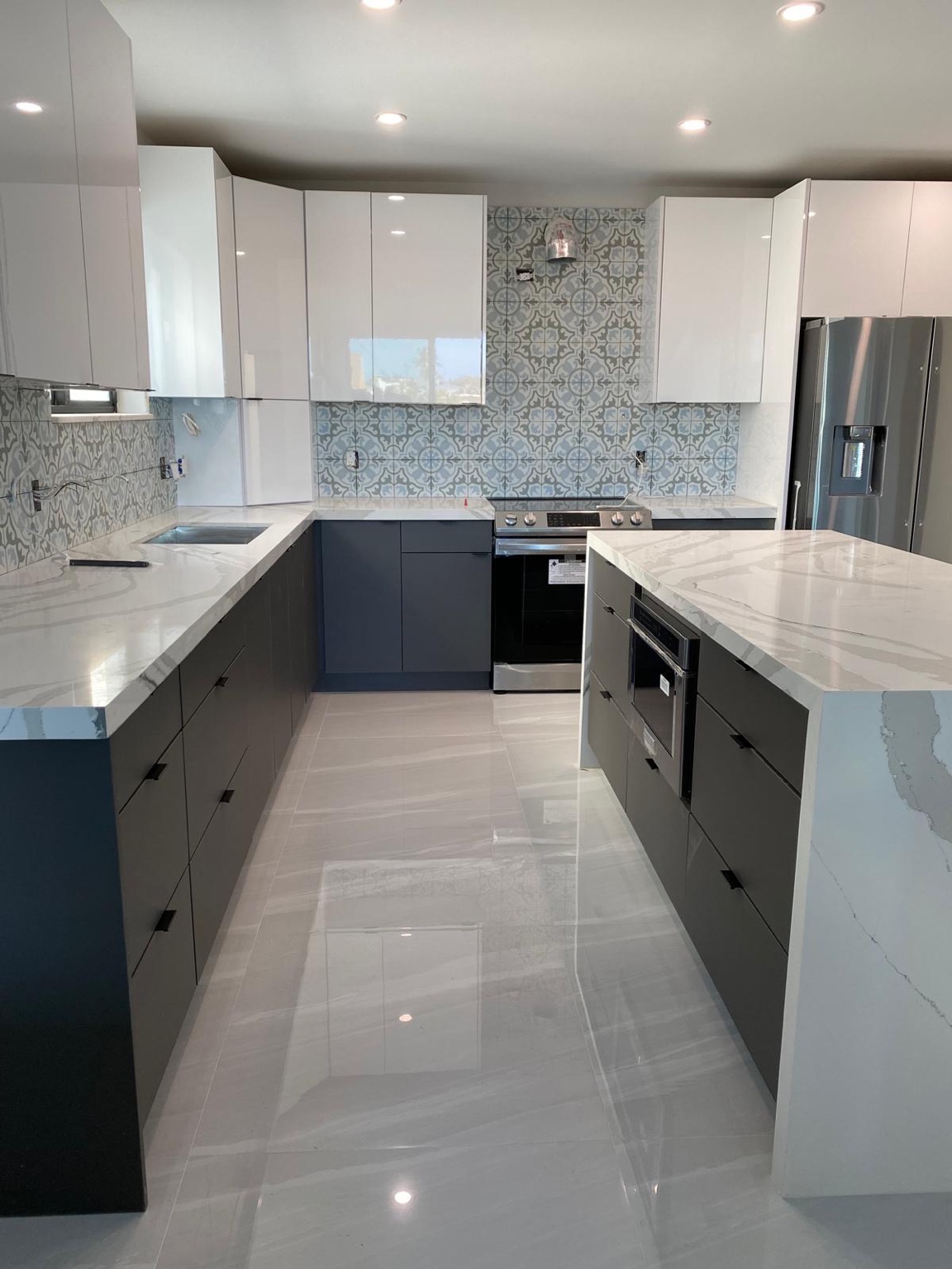 Kitchen renovation with white upper cabinets, dark lower cabinets, patterned backsplash, and a waterfall island